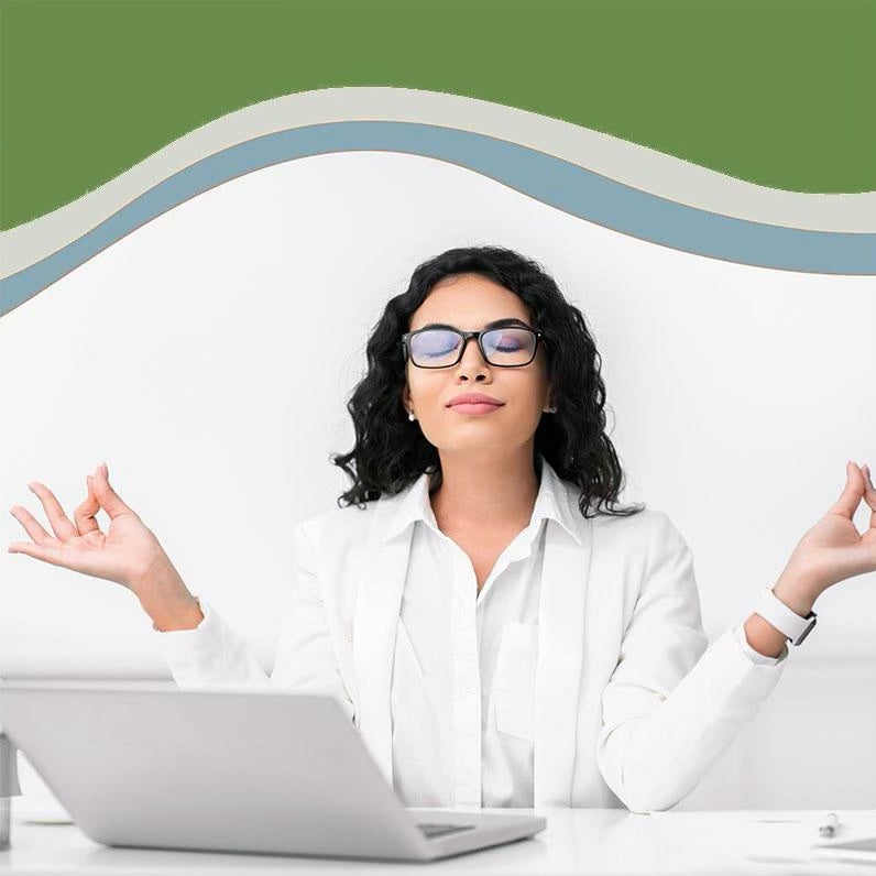 A woman wearing white sitting in her office with a peaceful expression on her face and her hands in a meditation mudra.