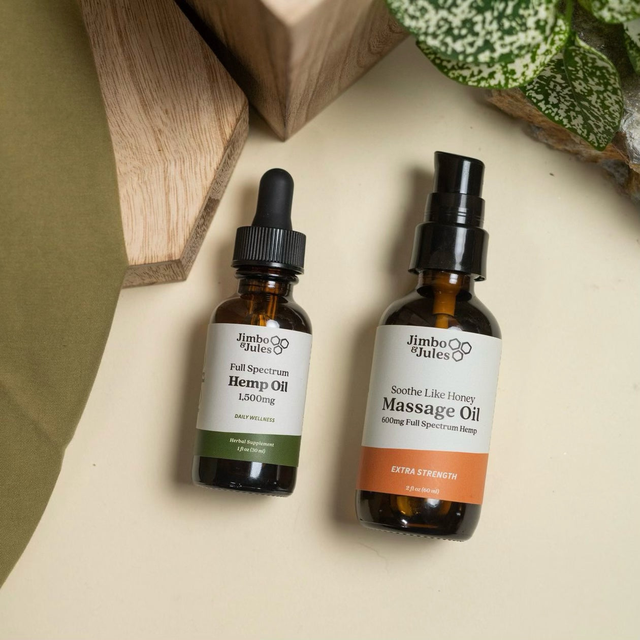 Jimbo & Jules 1,500mg Full Spectrum Hemp Oil and 600mg Full Spectrum CBD Massage Oil laying on a table next to a houseplant.