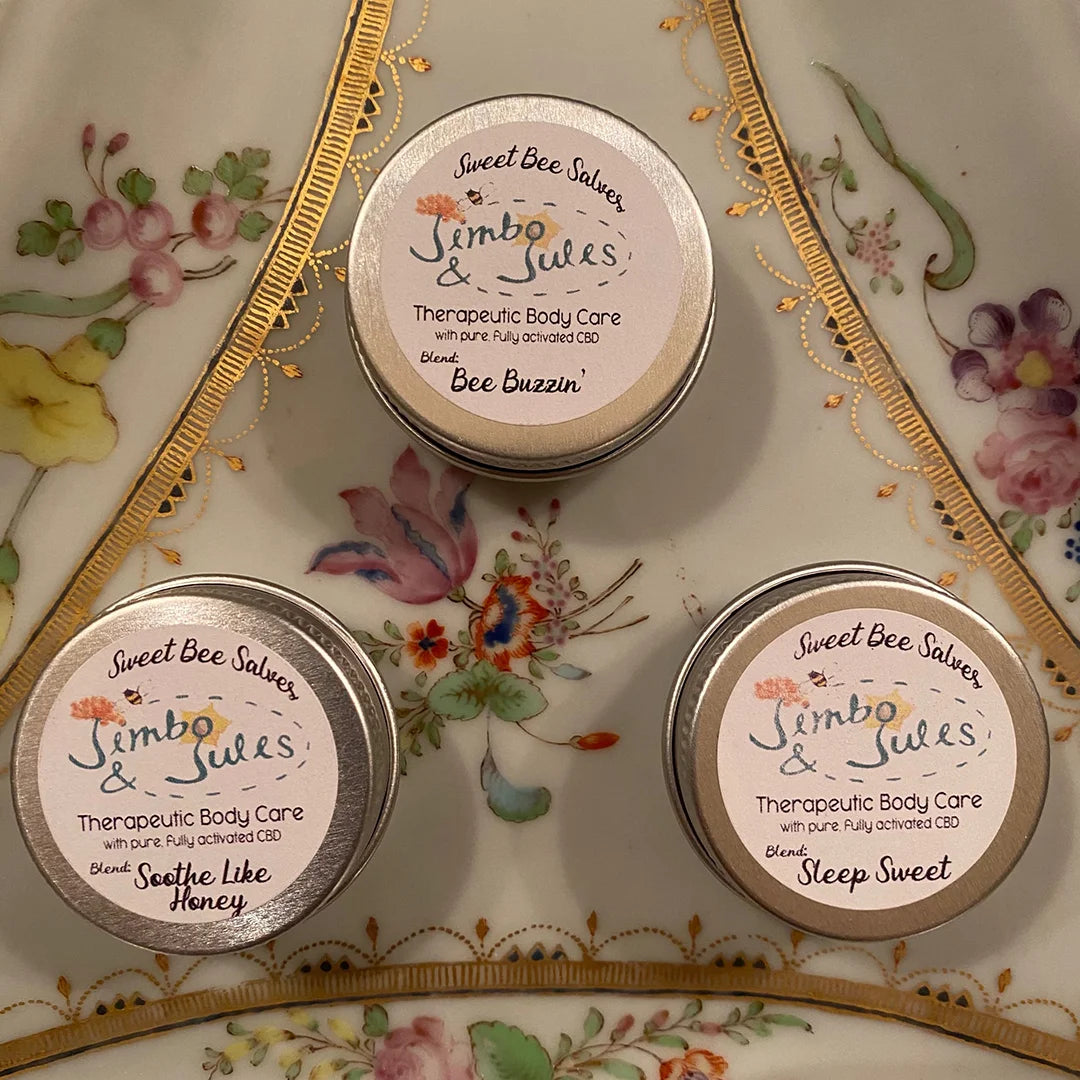Three small tins of Jimbo & Jules CBD salves arranged on a decorative floral plate.